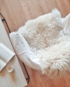 Dos corderitos de cuero de oveja color natural sobre un sillón, con un libro y una vela en una mesa de madera.