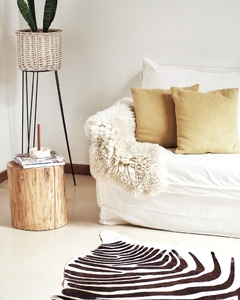 Un corderito de cuero de oveja color natural sobre un sofá blanco, con cojines amarillos y una mesa de madera al lado.