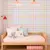 Papel de parede infantil xadrez vichy em tons pastel com cama de madeira clara e almofadas coloridas em quarto infantil