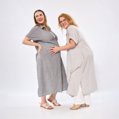 Mujer embarazada con vestido gris de rayas y mujer sonriendo con vestido claro y pantalones blancos, ambas posando en fondo blanco