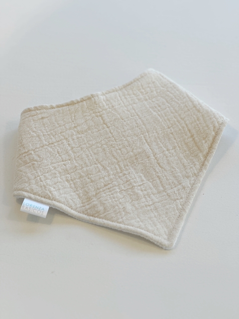Babero bandana de gasa tricapa impermeable en color natural, con textura suave y etiqueta visible.