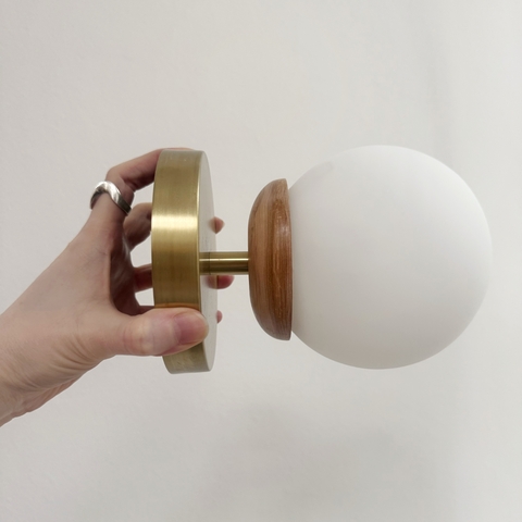 Aplique Lumi de pared o techo con base de metal dorado, detalle de madera y pantalla esférica blanca opaca