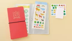 Carpeta Sticker File OTOÑO color rojo con elástico negro y otra gris abierta mostrando hojas plásticas con stickers coloridos de animales, árboles y otros diseños.