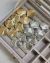 Brincos em metal com formato de conchas, disponíveis nas cores dourado e prateado, organizados em um porta-joias.