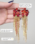 Brinco Lia dourado com pedrarias e strass vermelhos, franjas em correntes e fios de strass, ideal para festas e looks glamourosos"