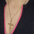 Colar dourado com pingente de cruz religiosa, exibido em um decote com zíper rosa.
