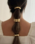 Elástico para cabelo dourado preso em um coque com três detalhes metálicos, visto de trás.