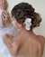 Mulher com cabelo cacheado preso, usando um arranjo com orquídeas brancas na parte de trás da cabeça.