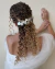 Arranjo prateado para cabelo de noiva com flores de petúnias, adornando um penteado com cachos soltos.
