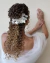 Arranjo para cabelo de noiva prateado com flores de petúnias, em cabelo cacheado, com fundo neutro.