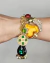 Pulseira dourada estilo vintage com berloques coloridos e pedrarias, destacando detalhes em forma de coração e estrela, vista no pulso.