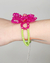 Pulseira flor brodada com cristais coloridos, apresentando detalhes em rosa e verde, usada em um pulso.
