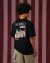 Camiseta preta oversized com estampa colorida de feira livre nas costas, usada por modelo de perfil