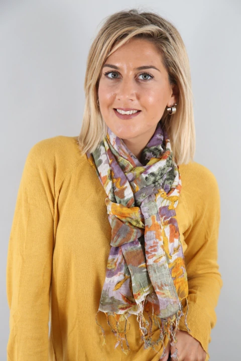 Mujer rubia con suéter amarillo usando pashmina estampada en tonos morados, naranjas y verdes