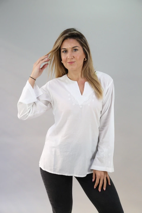 Mujer vistiendo blusa blanca de manga larga con bordados sutiles en el pecho y las mangas, combinada con pantalones oscuros