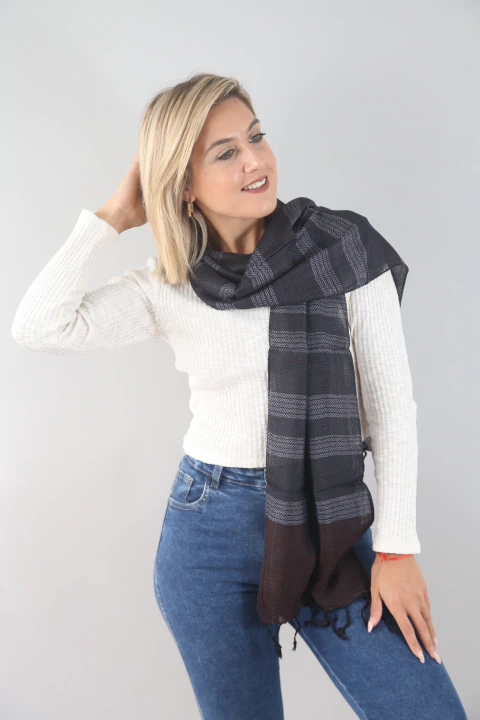 Mujer usando una pashmina negra con detalles en gris, vestida con un suéter blanco y jeans azules, sonriendo.