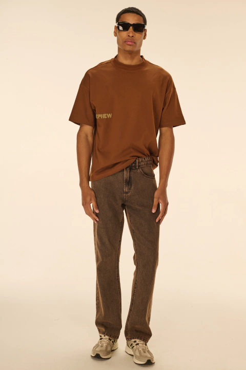 Homem usando calça jeans marrom boot cut Nephew com camiseta marrom e tênis brancos