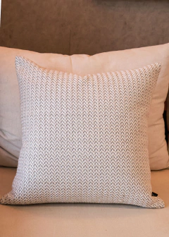 Almofada quadrada em linho offwhite com padrão zig zag, posicionada sobre um sofá claro.