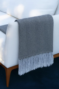 Manta de tear em algodão cinza com padrão geométrico pendurada no braço de um sofá branco