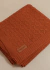 Manta Tricot Entrelace na cor cobre, com textura trançada e etiqueta da marca Cazachic.