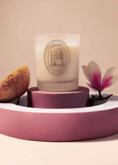 Vela perfumada Magnólia Pacífica em um suporte decorativo com elementos florais e uma fruta ao lado.