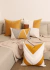 Conjunto de almofadas em tons de caramelo e offwhite sobre um sofá, incluindo uma almofada retangular bordada.