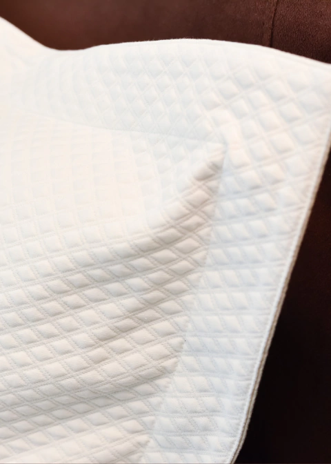 Capas de travesseiro em matelassê branco, com textura em formato quadriculado, sobre um fundo marrom.