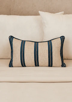 Almofada retangular com listras azul marinho e cru, colocada sobre cama com roupas de cama em tons neutros