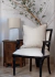 Almofada Arminho em uma cadeira elegante ao lado de uma mesa com um abajur e uma planta decorativa.