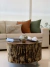 Conjunto de almofadas decorativas em um sofá claro, com estampas de folhas e em cores terrosas, sobre uma mesa de centro de madeira rústica.