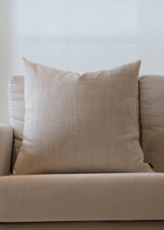 Almofada quadrada em linho tramado na cor offwhite, posicionada sobre um sofá claro.