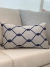 Almofada retangular azul decorativa com padrão em jacquard, posicionada sobre um sofá claro.
