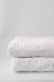 Cobre leito branco em camadas, com textura suave e costura em padrão de losangos.