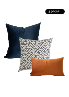 Kit com três almofadas, uma azul escura lisa, uma com estampa geométrica azul e branca, e uma retangular cobre lisa