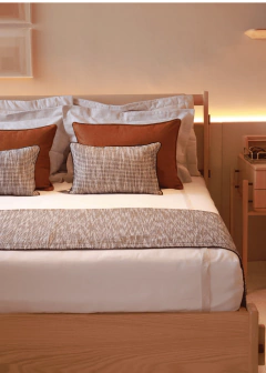Peseira Austrália em tons preto e cinza sobre cama de madeira com travesseiros marrons e almofadas decorativas