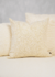 Almofada offwhite com textura suave em um sofá, parte de um kit de três almofadas.
