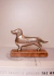 Escultura de cachorro em metal prateado sobre uma base de madeira.
