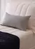 Almofada retangular listrada em preto e branco sobre uma cama com roupa de cama clara.