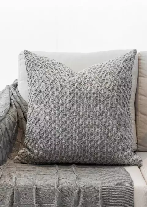 Almofada em linho bordado na cor cinza claro, com padrão texturizado, colocada sobre um sofá.