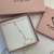 Pulseira de mão em ouro com design delicado e pingentes de ponto de luz, apresentada em caixa rosa