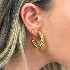 Brinco de argola torcida dourada usado na orelha de mulher com cabelo loiro