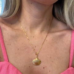 Colar dourado com pingente em formato de concha usado no pescoço de mulher com vestido rosa