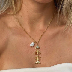 Colar dourado com pingente em formato de espinha de sardinha e detalhe de pérola, usado no pescoço de mulher