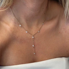 Colar gravata feminino Yara em ouro com pequenos pontos de luz brilhantes, usado no pescoço de uma mulher