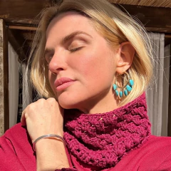 Mulher loira usando brinco argola com pedras turquesa e blusa de gola alta rosa