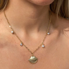 Colar dourado com pingente de concha e pequenas pérolas usadas no pescoço de mulher