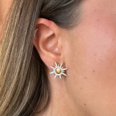 Brinco Sun Duo em formato de sol com centro dourado e raios cravejados com zircônias cristais, usado na orelha de mulher