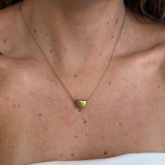 Colar delicado com pingente em formato de círculo fosco em tom dourado usado no pescoço de uma mulher