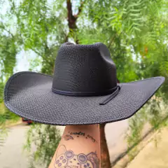 Chapéu Eldorado Mexicano Strongs Black, modelo preto, segurado por uma mão com tatuagens, em um ambiente externo com árvores ao fundo.