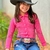 Menina sorridente usando um body feminino de manga longa rosa com brilho, combinado com um cinto e chapéu de cowboy.